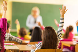 Rear view of school kids raising their hands at school
