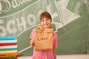 Schoolgirl holding sack lunch in classroom